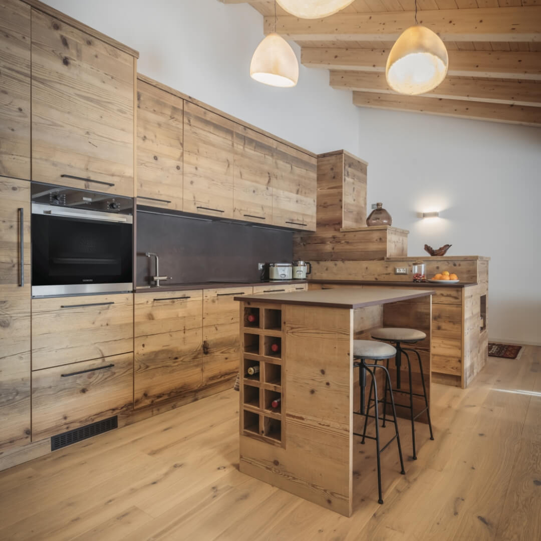 Cucina in legno di montagna grezzo con isola centrale con sgabelli alti e porta bottiglie